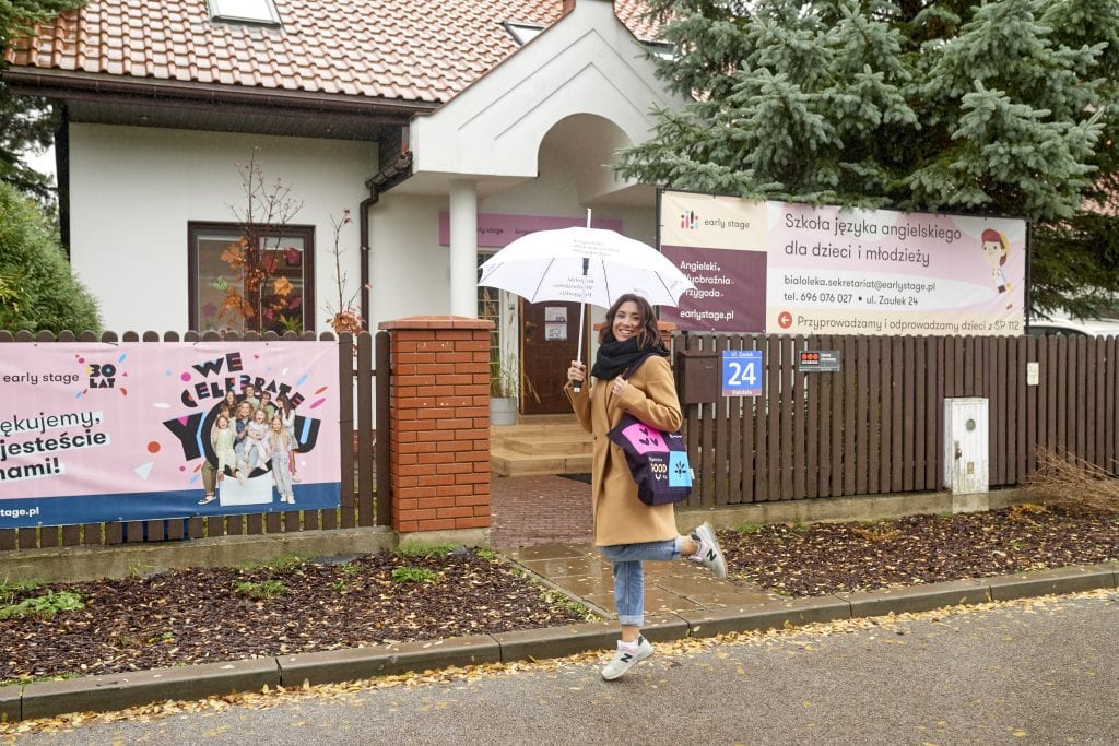 Szkoła języka angielskiego Early Stage. Przed budynkiem stoi franczyzobiorczyni z parasolką